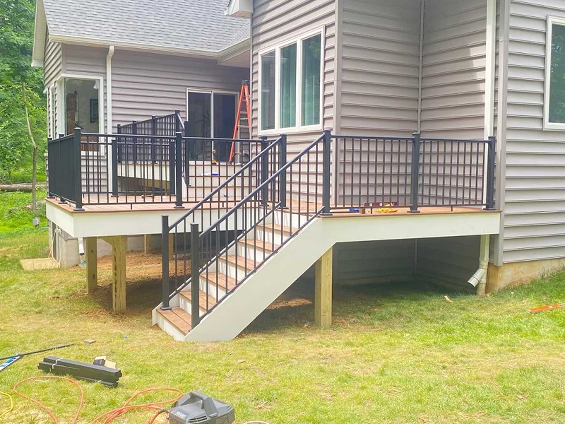 New deck with black railings and stairs attached to a gray house, set in a grassy backyard.