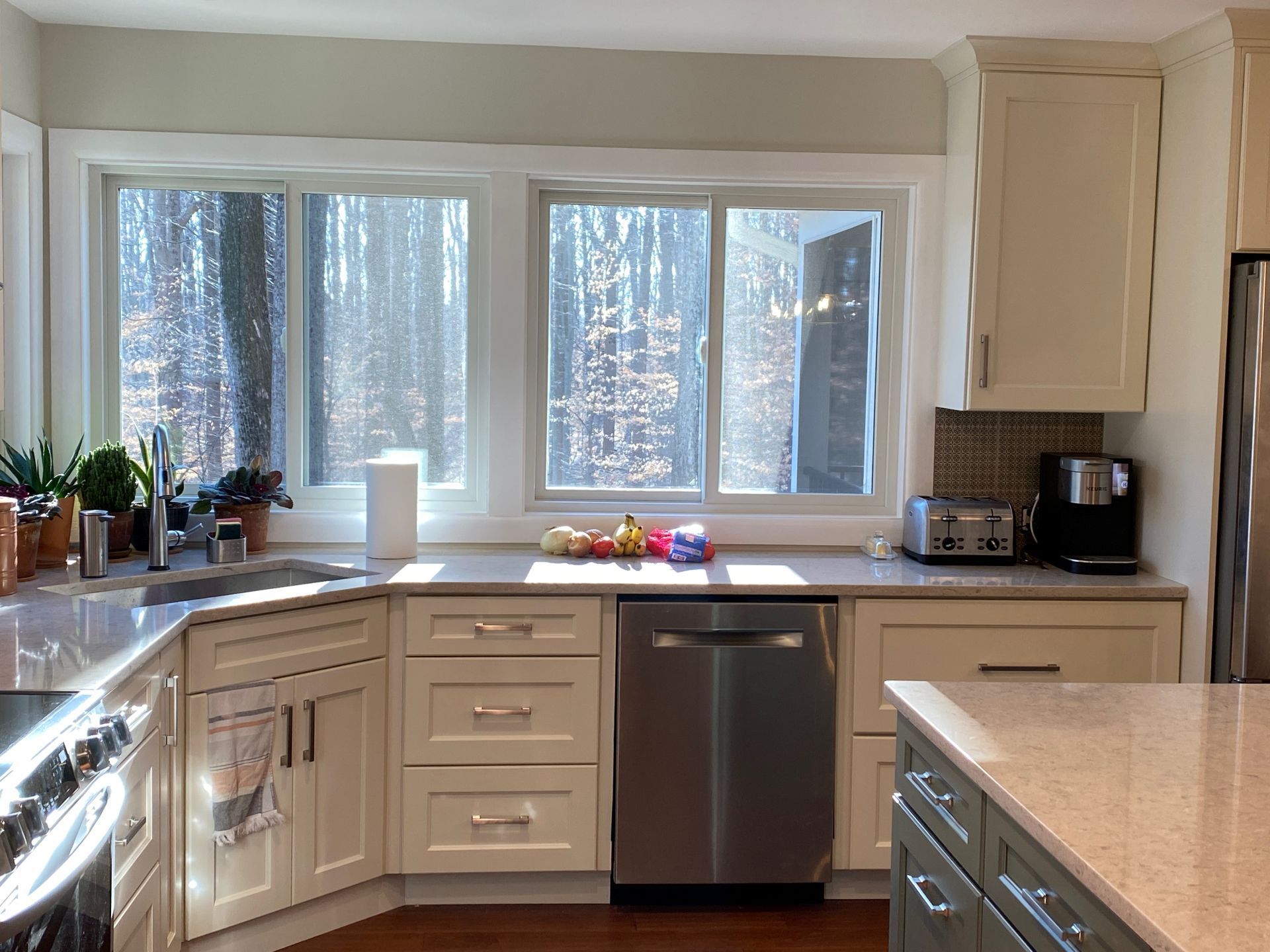 Kitchen with white cabinets, stainless steel appliances, and a window overlooking trees.