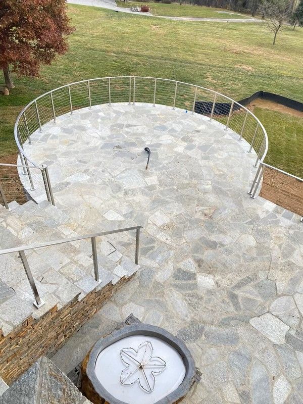 Stone stairs leading up to a circular platform with a metal railing, overlooking a green landscape.