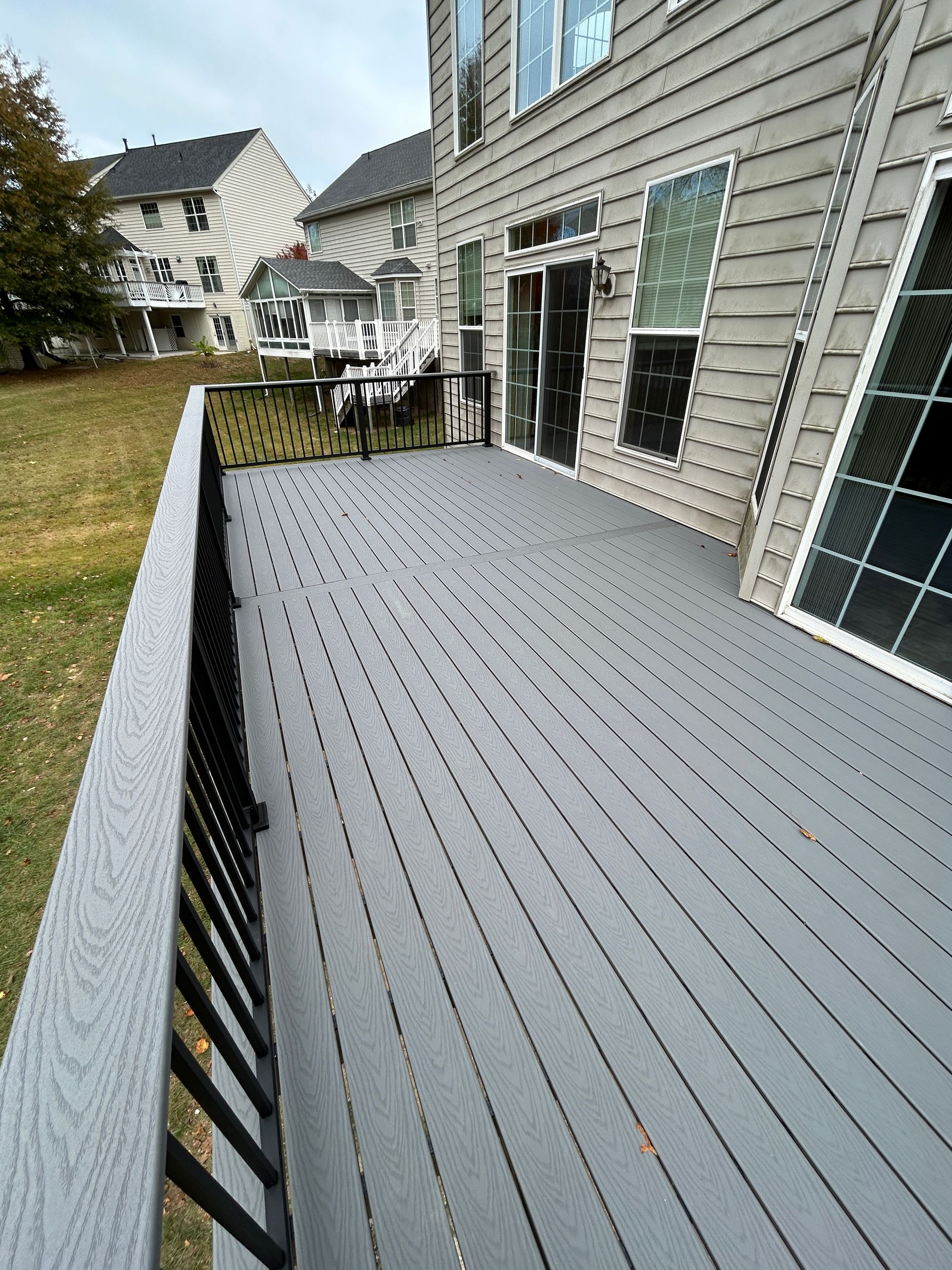 Grey composite deck with black railing next to a house with large windows.