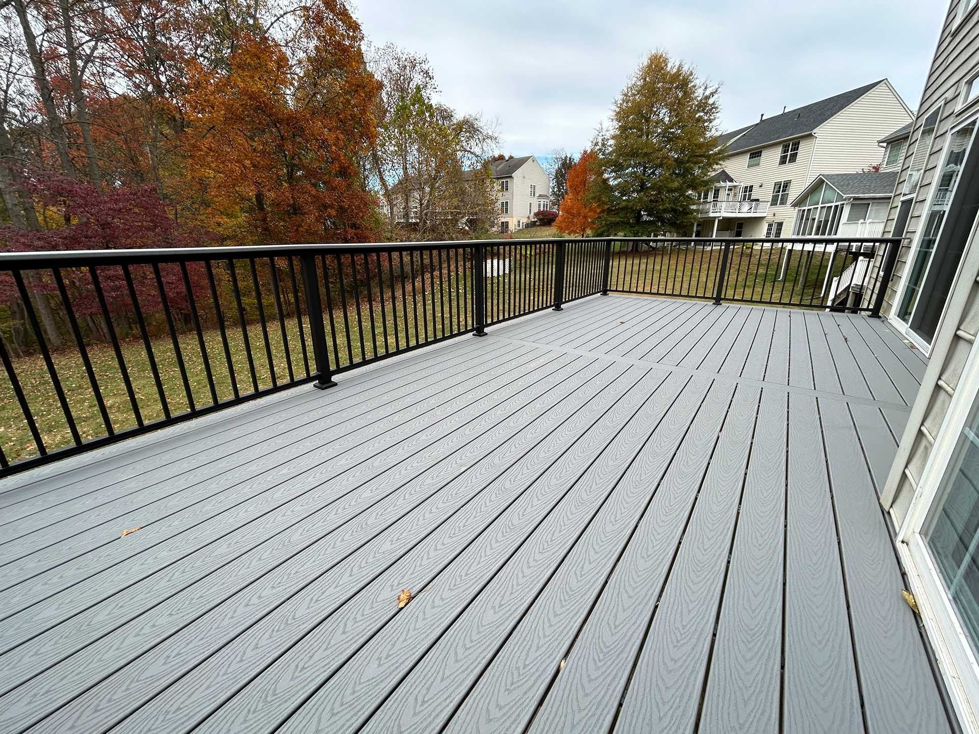 Gray composite deck with black railing overlooking a yard with trees showing autumn colors.
