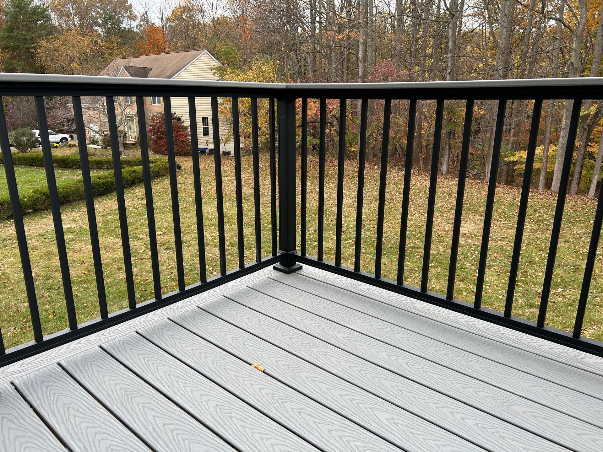 Black metal deck railing on a gray composite deck, overlooking a backyard with fall foliage.