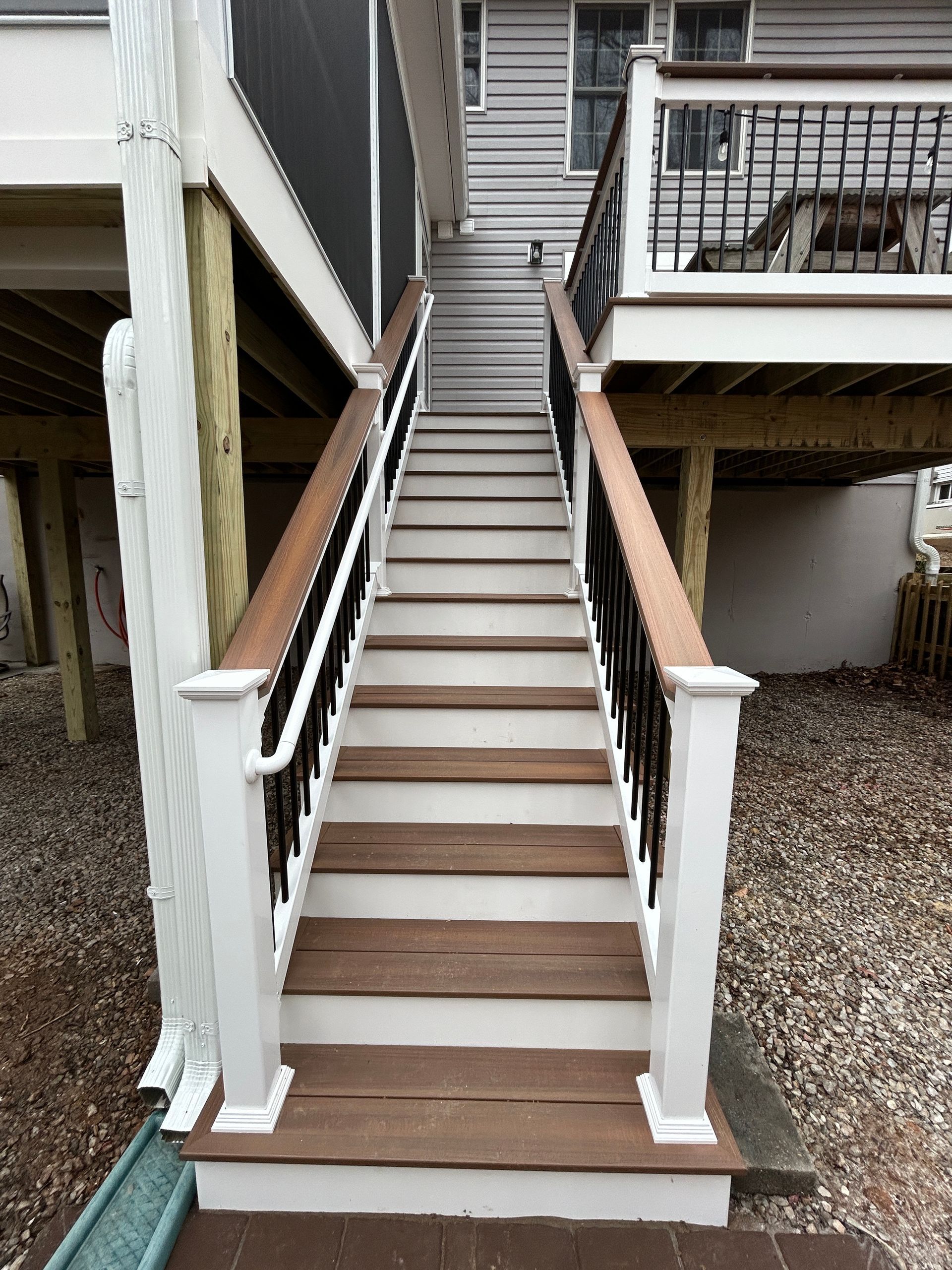 Wooden outdoor staircase leading up to a deck, with white and black railings, surrounded by gravel.