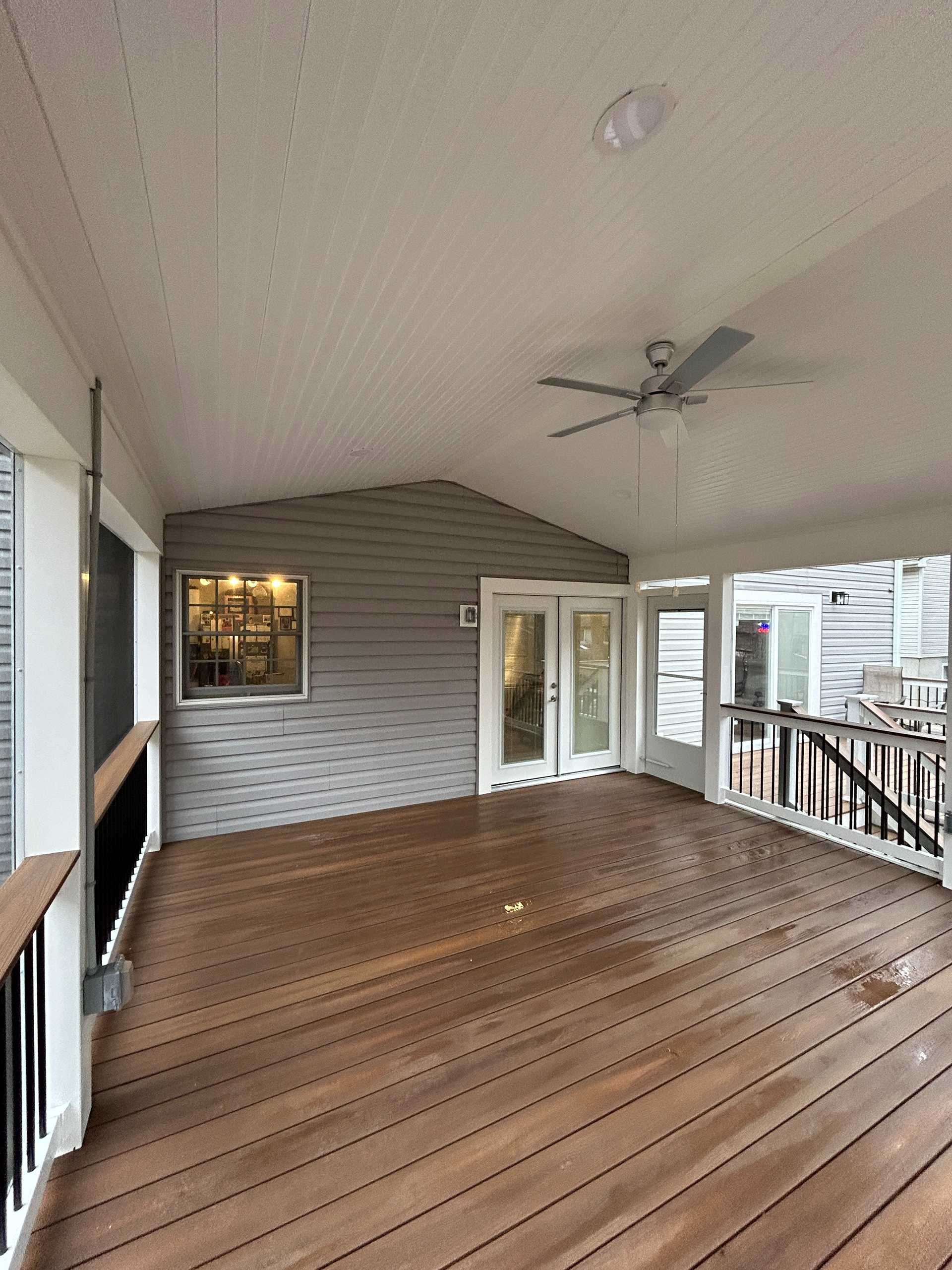 Covered porch with wood deck, light gray siding, and a ceiling fan.