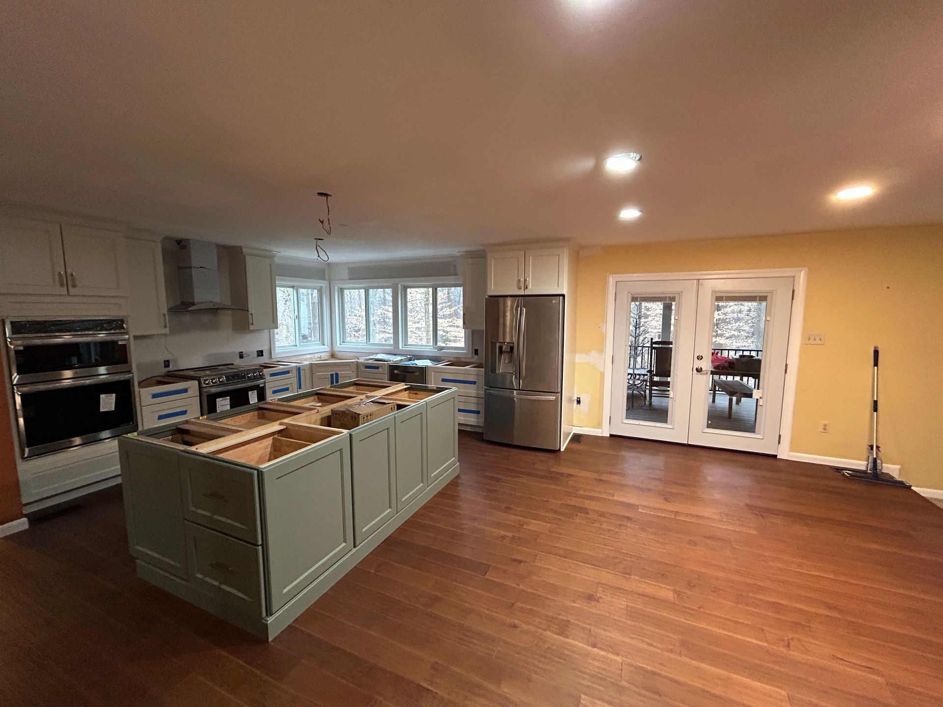 Kitchen renovation in progress: cabinetry in place, island, stainless steel appliances, hardwood floor, light fixtures.