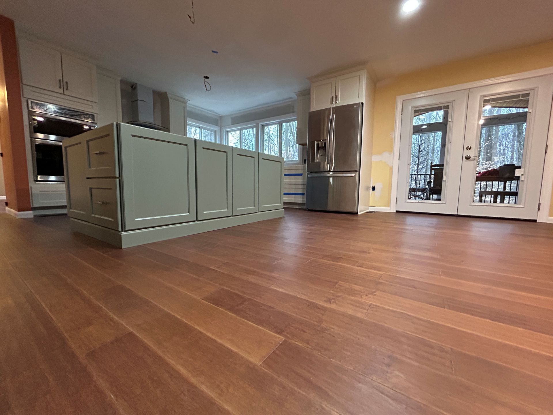 Kitchen with green island, stainless steel refrigerator, white cabinets, and wood flooring.