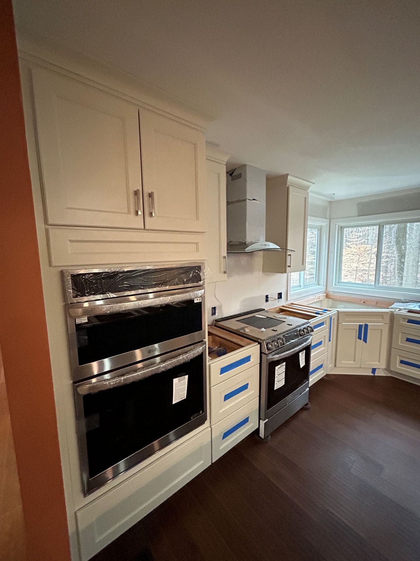 Cream-colored kitchen cabinets with stainless steel oven and range, dark wood floor, and range hood.