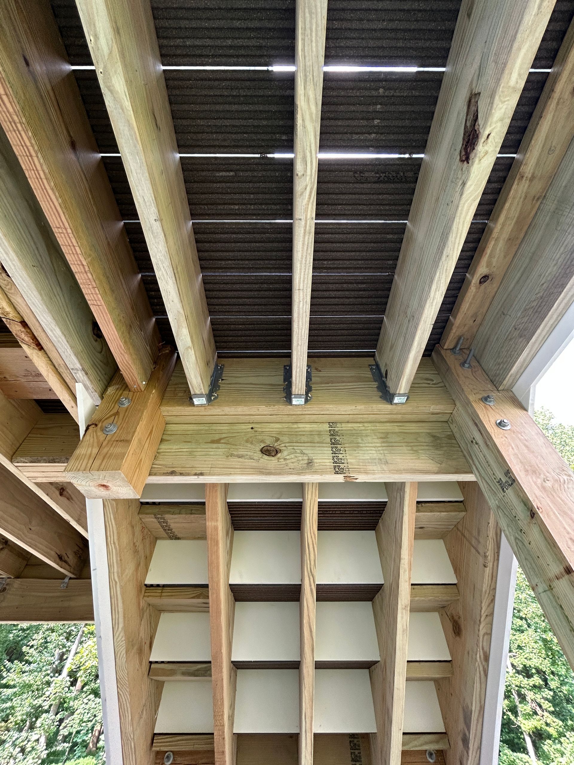 View from below a wooden deck showing beams, support structure, and deck boards.