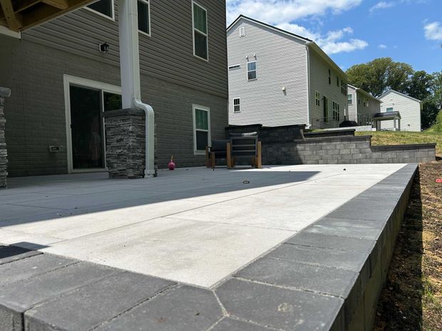 Concrete patio with dark border next to a house and retaining wall.