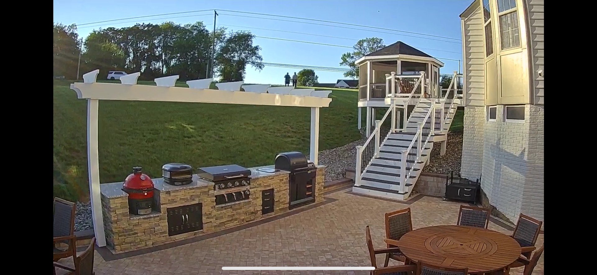 Backyard patio with outdoor kitchen, dining table, and raised gazebo with stairs.