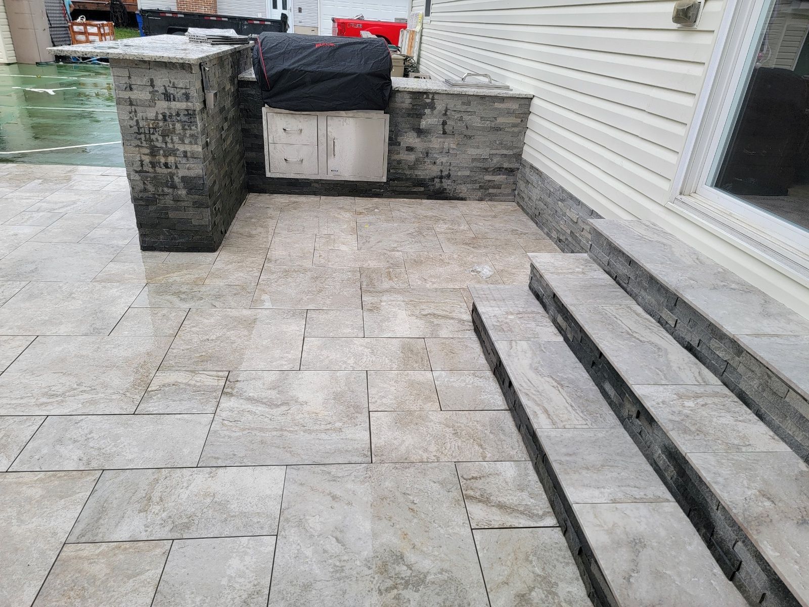 Outdoor patio with stone pavers, built-in grill area, and steps leading to a door.