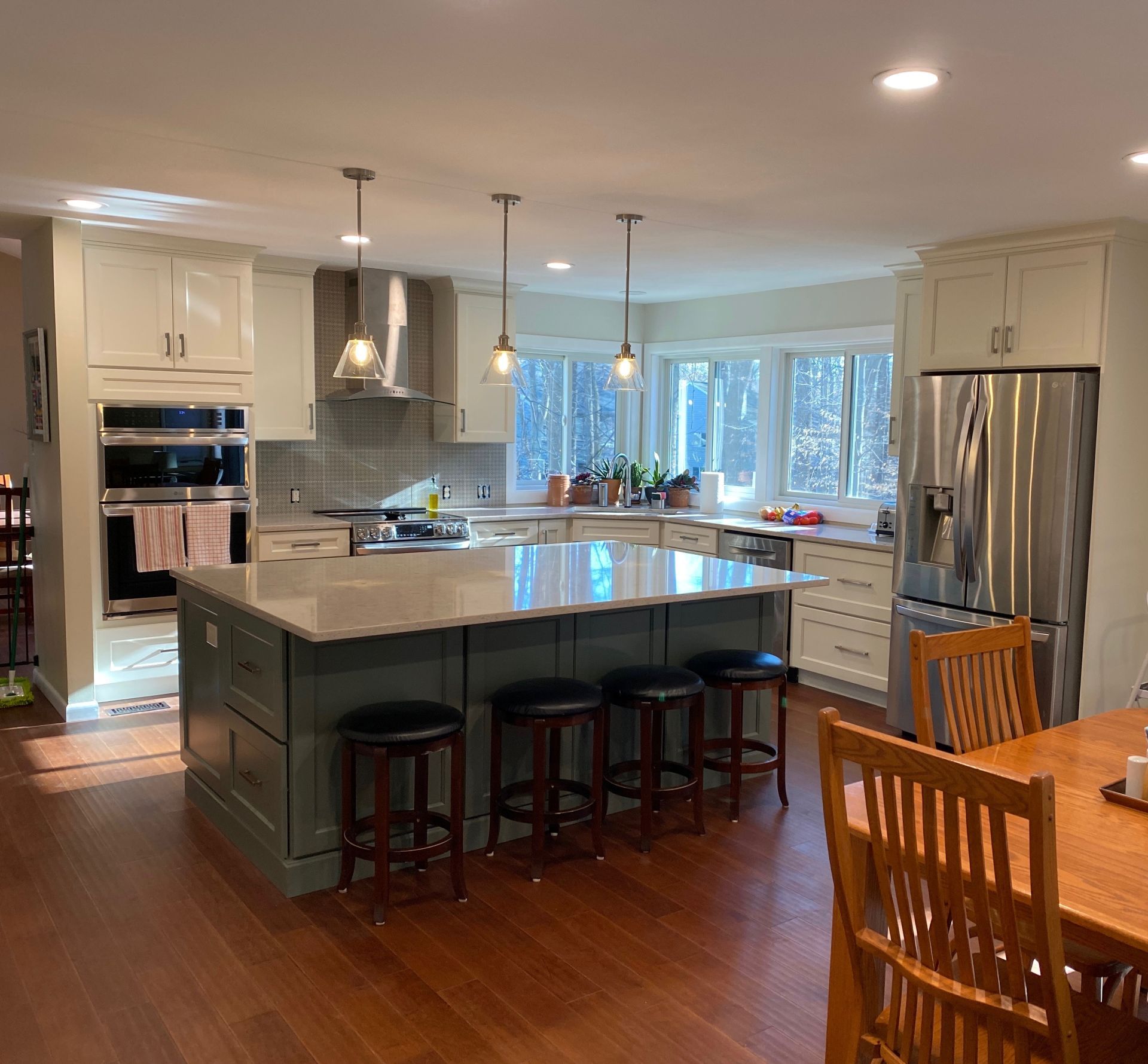 Kitchen with green island, light cabinets, stainless steel appliances, and wood floor.