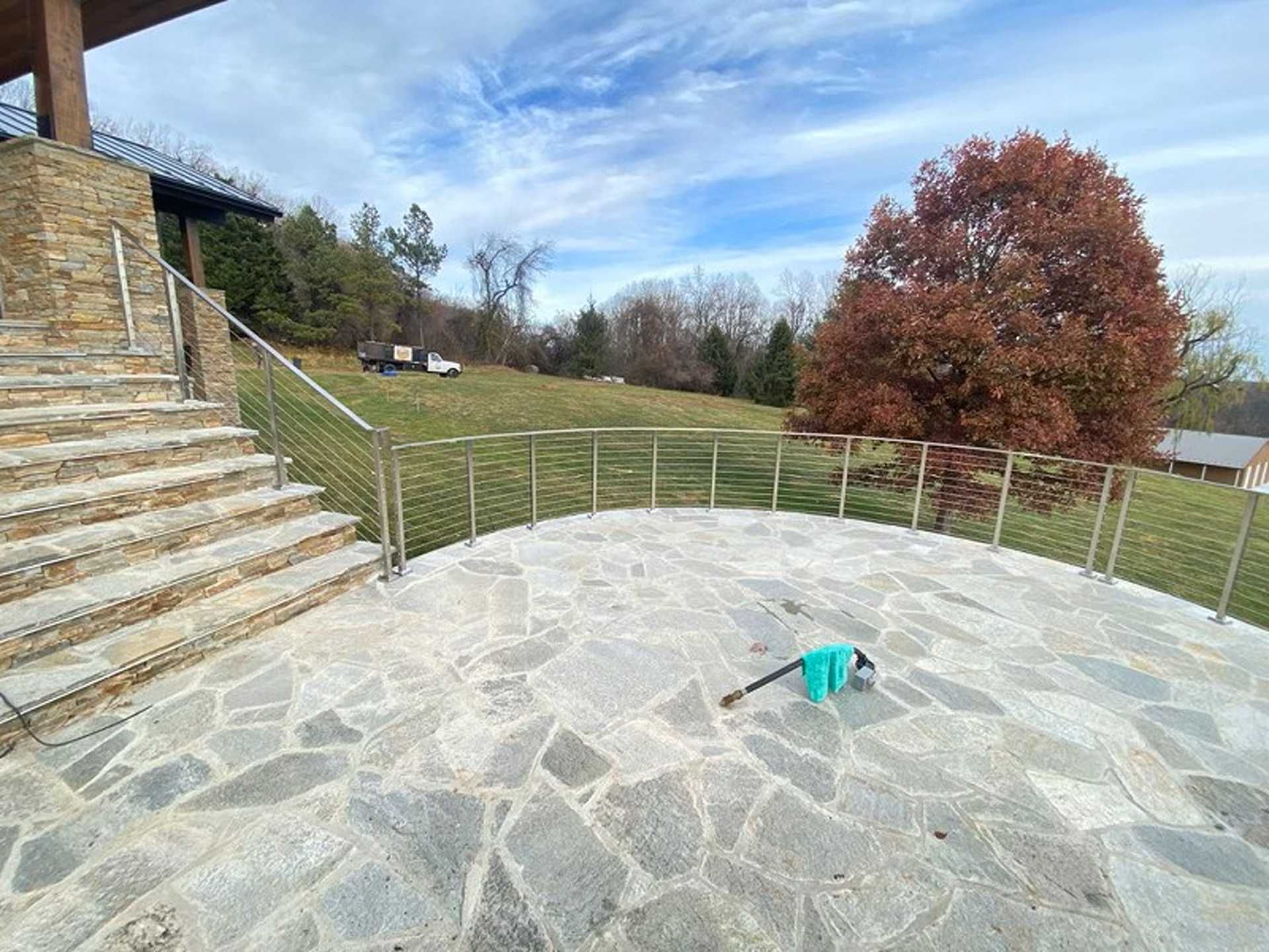 Stone patio with stainless steel railing and steps, overlooking a grassy hill and autumn tree.
