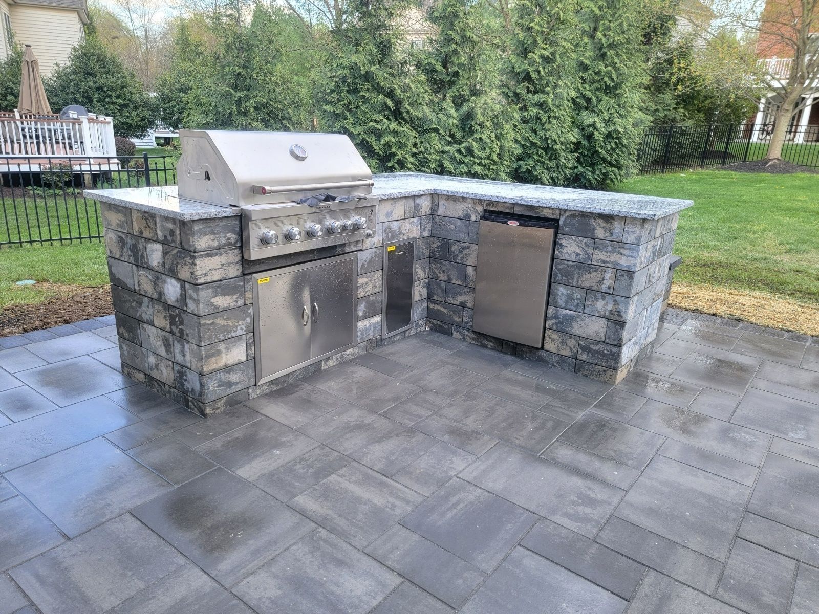 Outdoor kitchen with a grill, refrigerator, and stone facade on a paved patio.