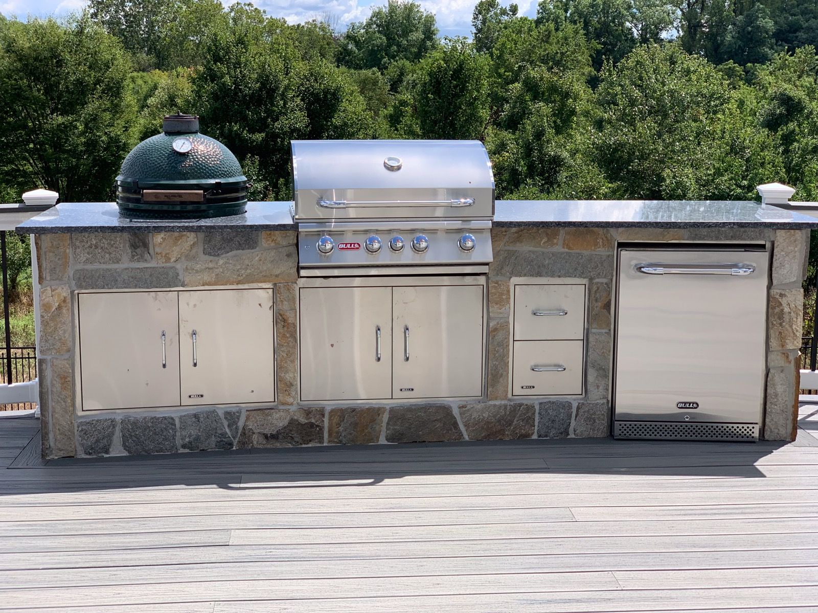 Outdoor kitchen with a Big Green Egg, grill, refrigerator, and storage cabinets, built into a stone countertop.