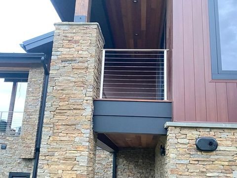 Exterior of a modern home with stone columns, wood siding, and a balcony with horizontal steel cable railing.