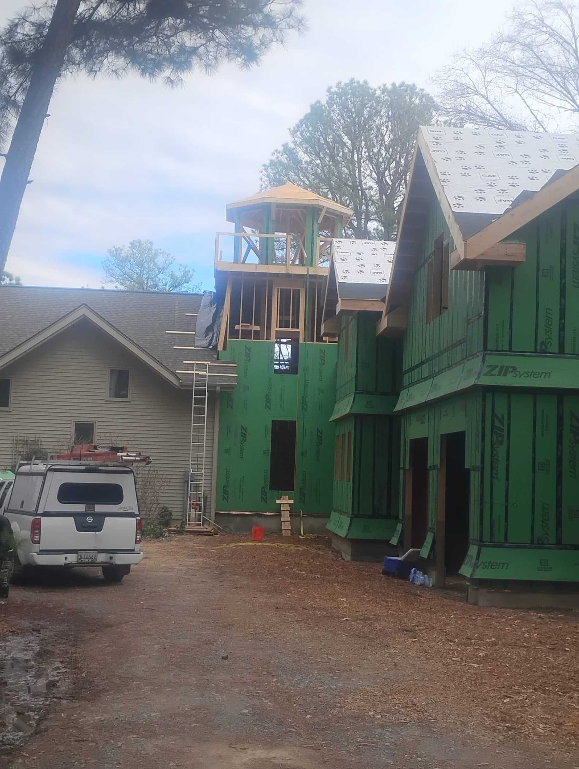 Construction site: partially built house with green siding, a small turret, and a pickup truck.