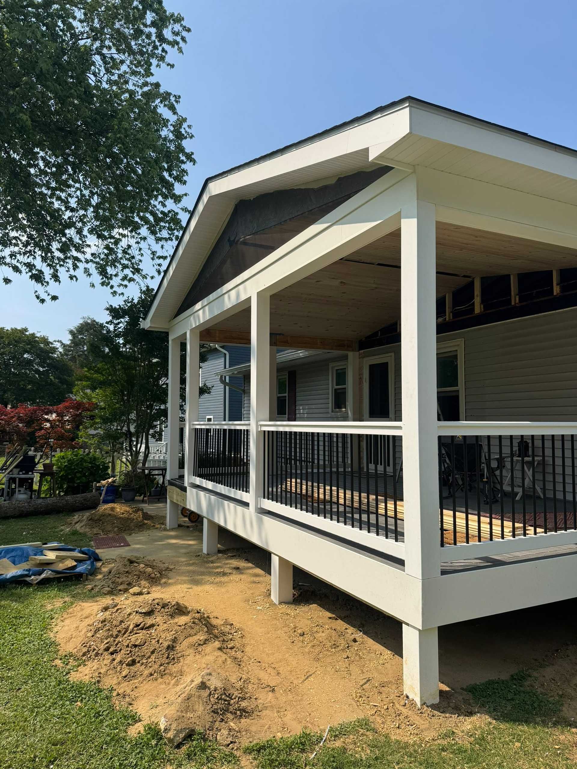 Newly built white porch with black railing and off-white columns, under a roof, and an open dirt area.