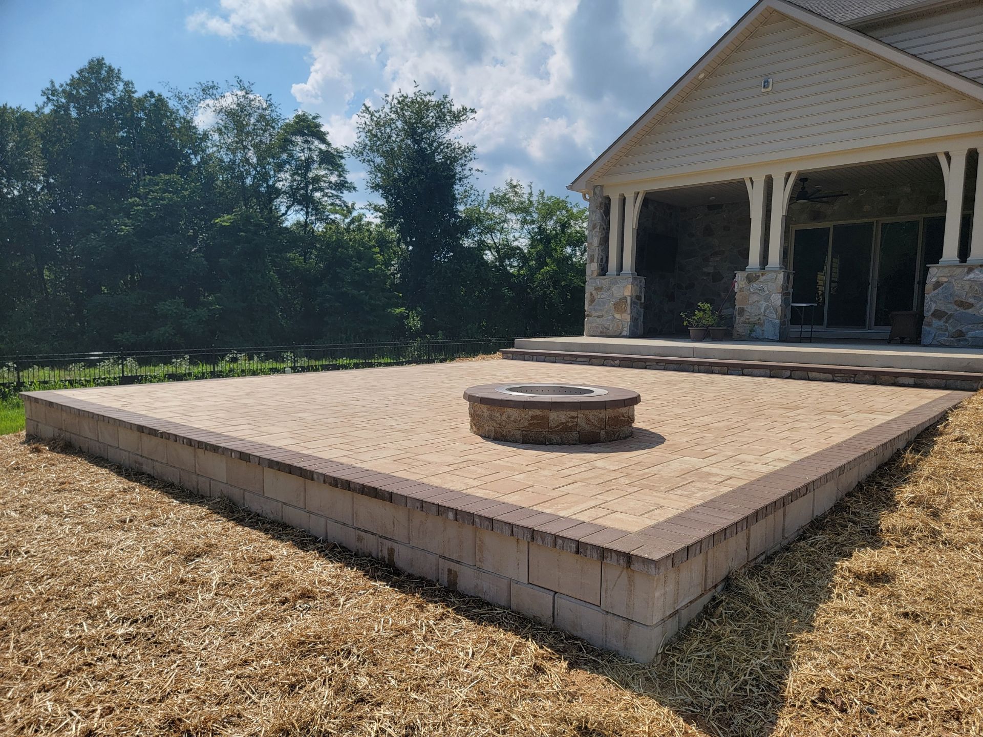 Brick patio with fire pit in front of a house with a covered porch.
