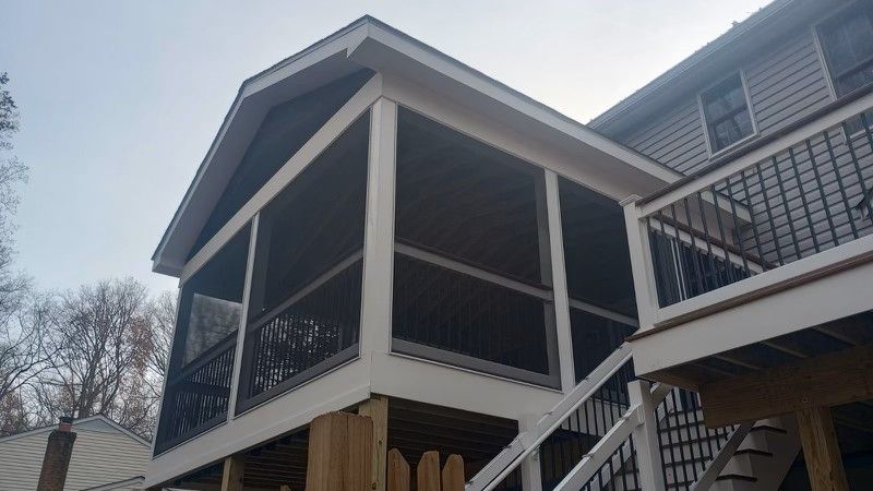 Screened-in porch addition with white trim, dark screens, and deck with stairs, attached to a house with gray siding.