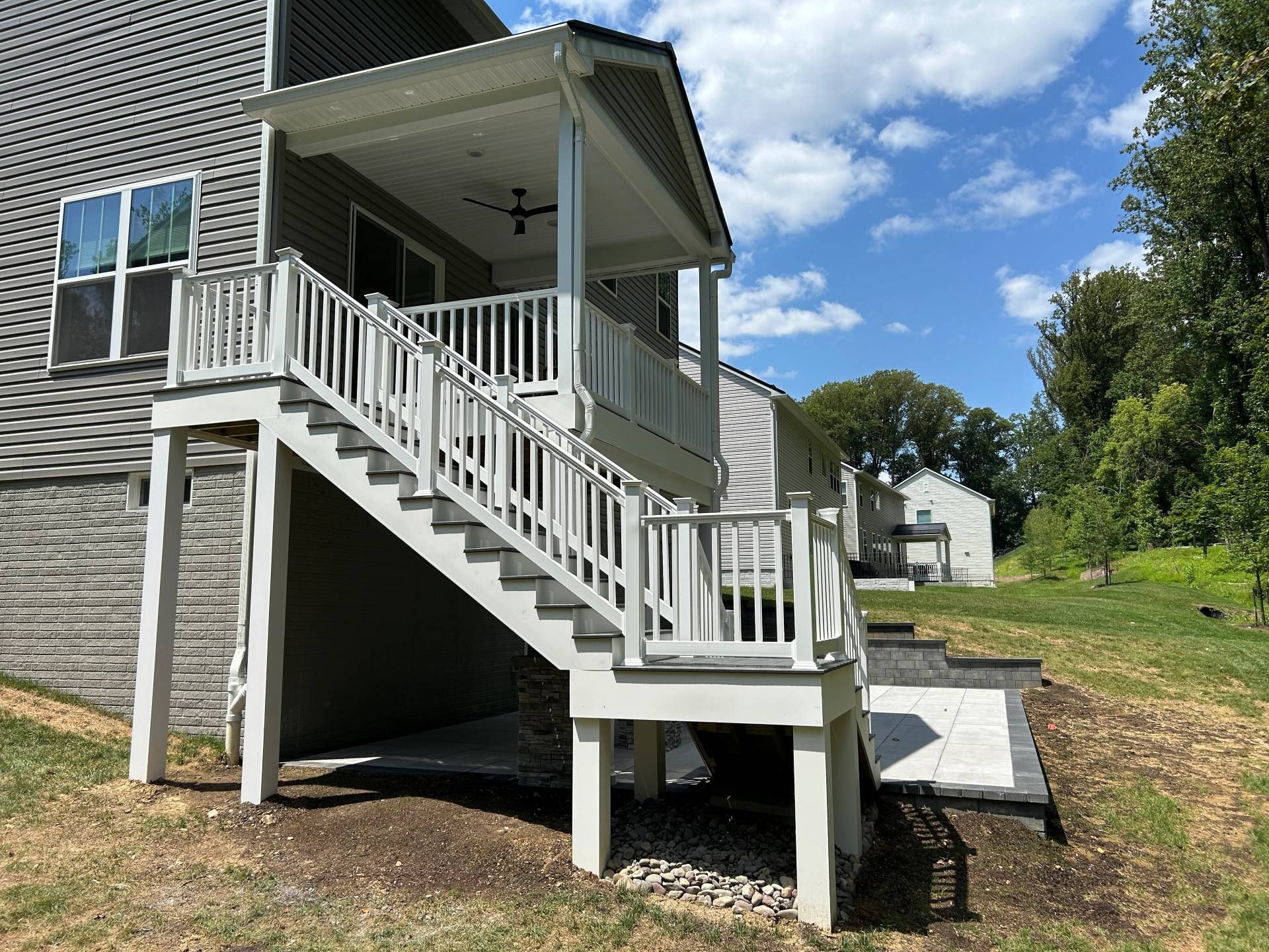 Gray deck with stairs leading to a covered porch; the scene is outdoors on a sunny day.