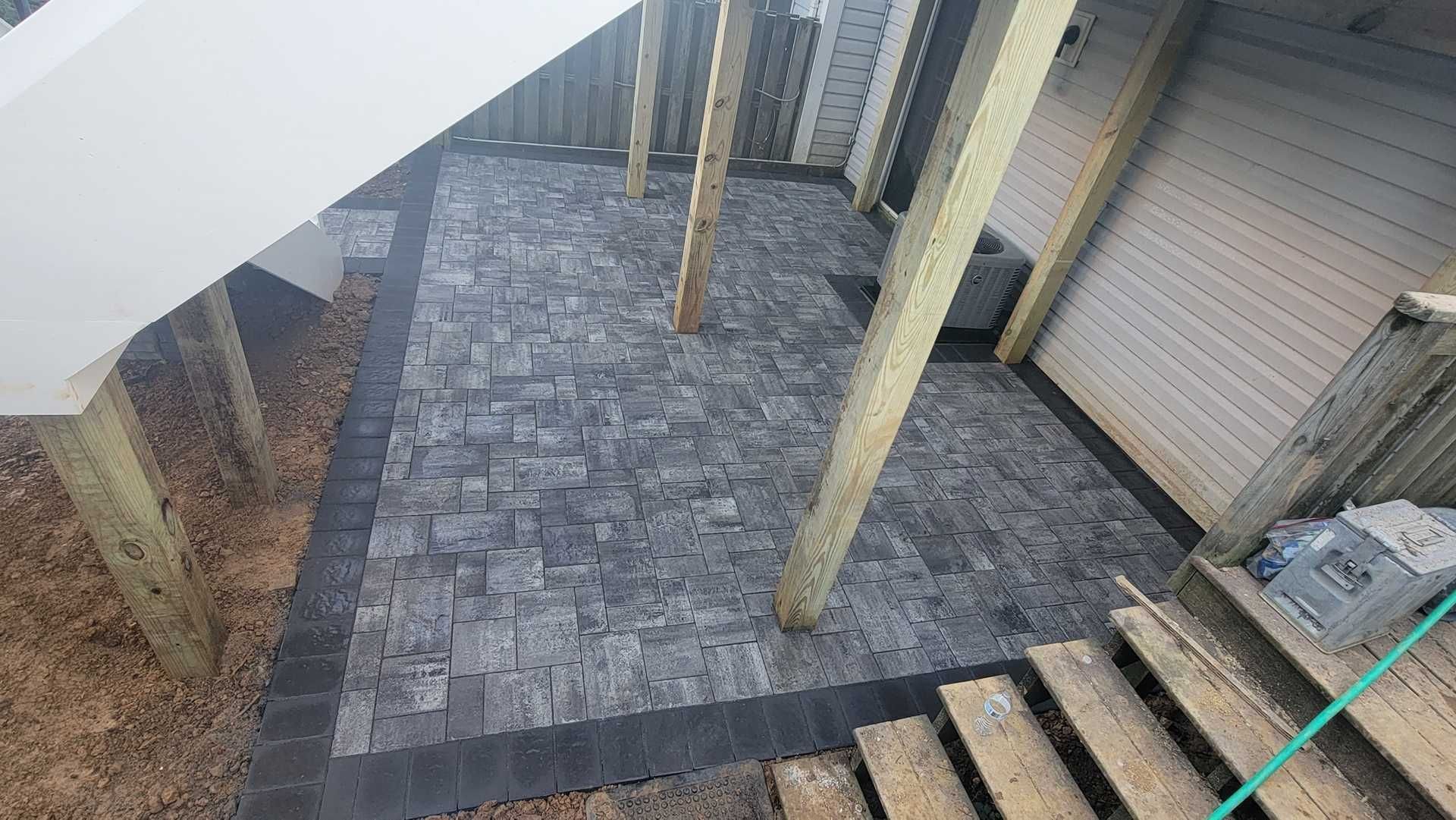Stone patio under a wooden deck, bordered with darker stones. Support beams and stairs visible.