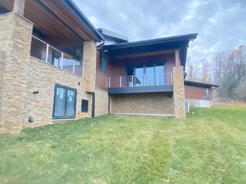 Exterior of a modern house with stone facade, glass doors, and a grassy yard under a cloudy sky.