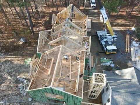 Construction site: wooden house frame with crane. Green walls, workers, and a truck visible.