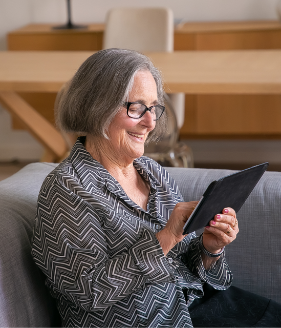 Elderly woman using an ipad while sitting on a couch.