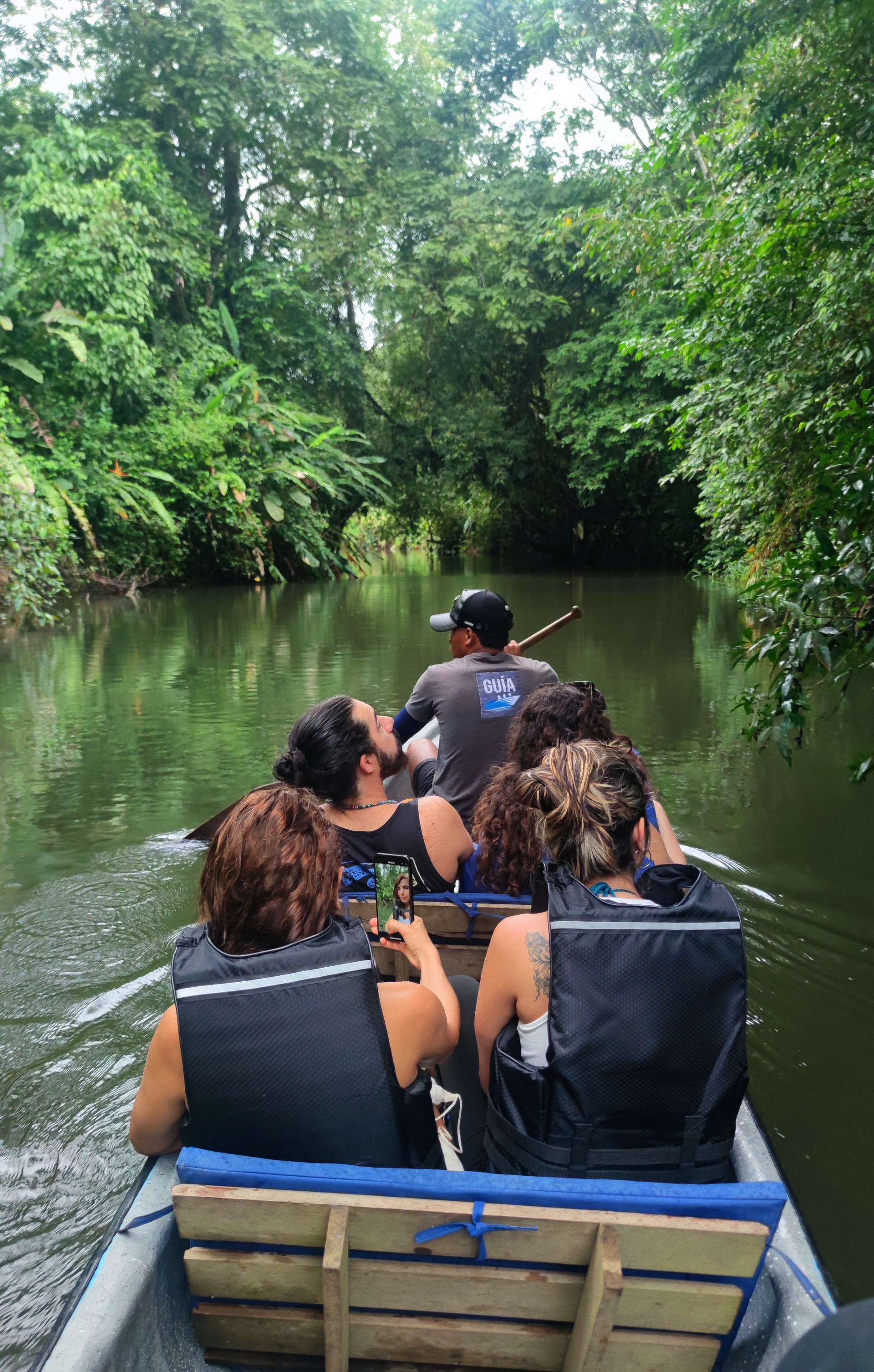 People riding in a small boat through a narrow, tree-lined river channel