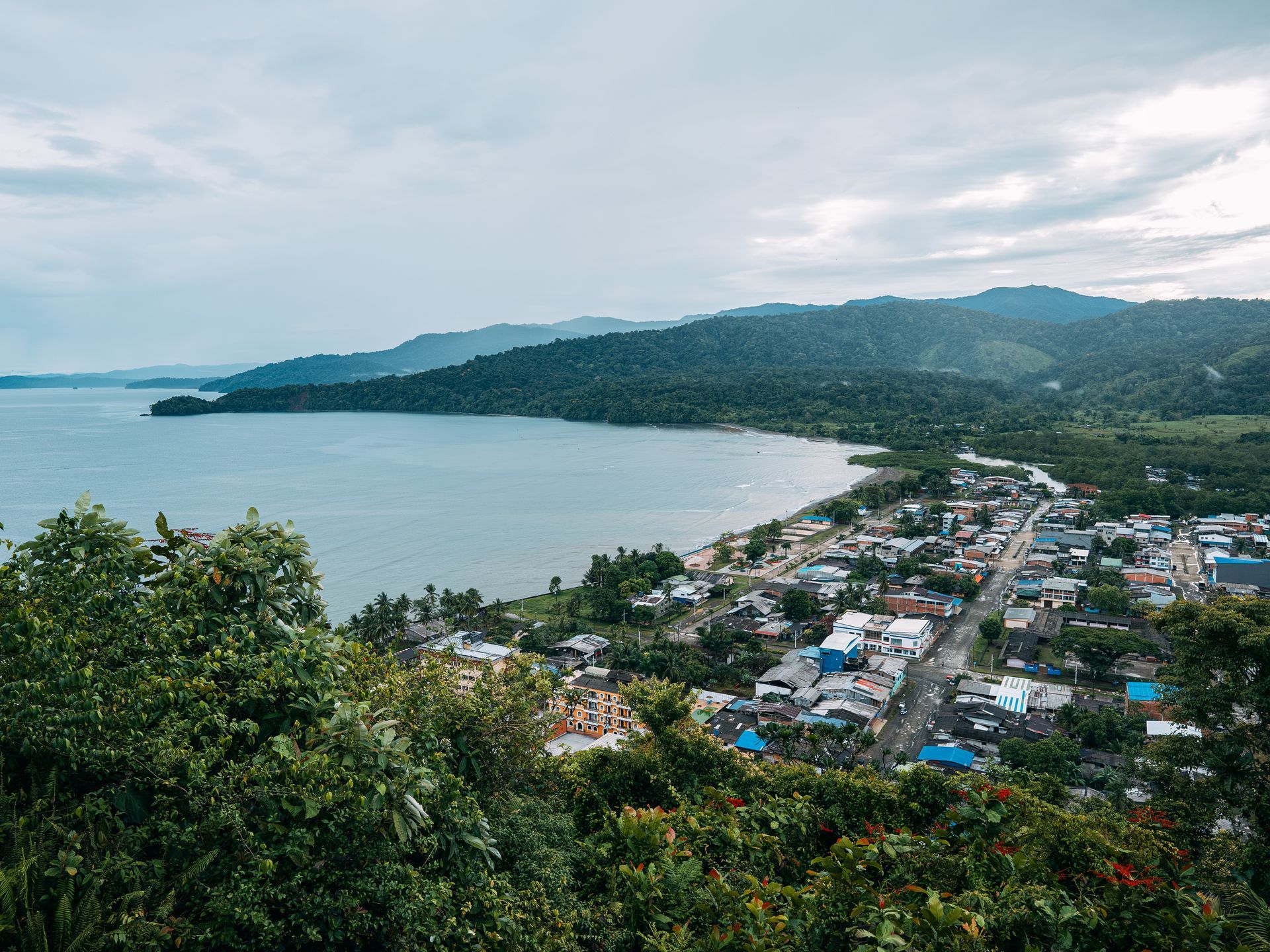 Coastal town beside a bay, with green hills and cloudy sky overlooking the shoreline