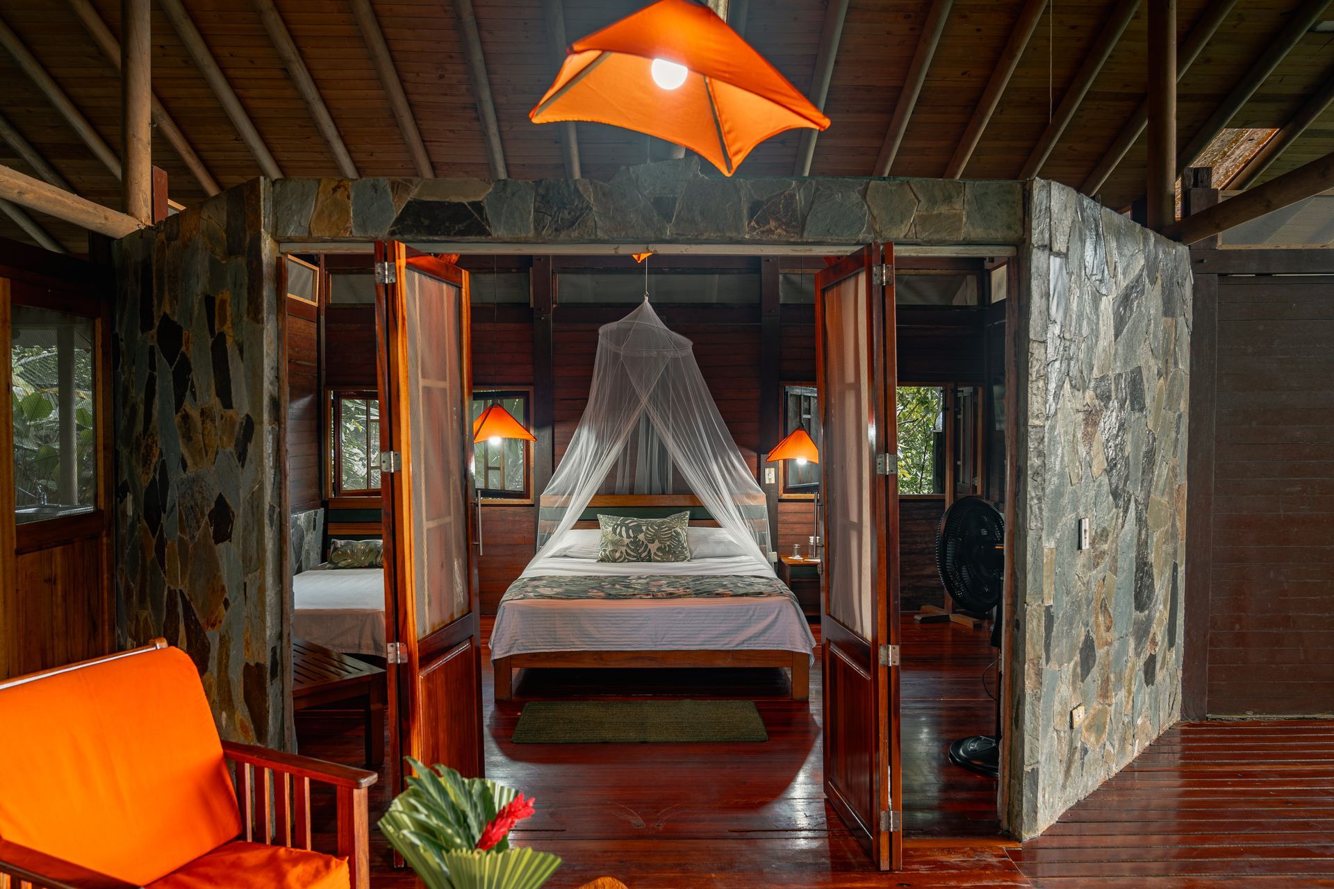 Orange-accented resort bedroom with four-poster bed, mosquito net, and open wooden doors
