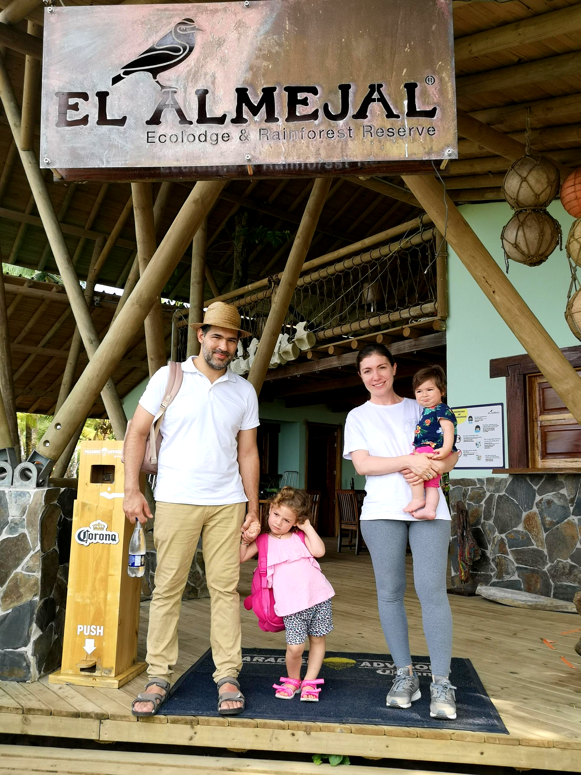 Family posing outside El Almejal entrance sign, with adults and two children under a rustic wooden canopy.