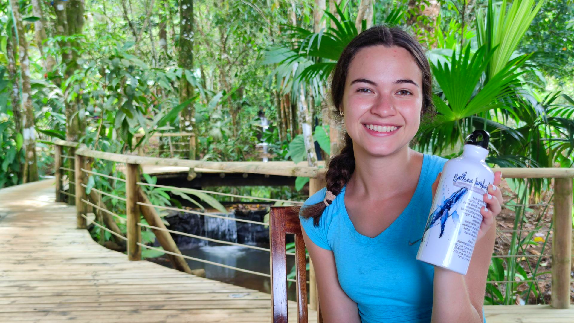 Smiling woman in blue shirt at a wooden walkway in a lush tropical forest