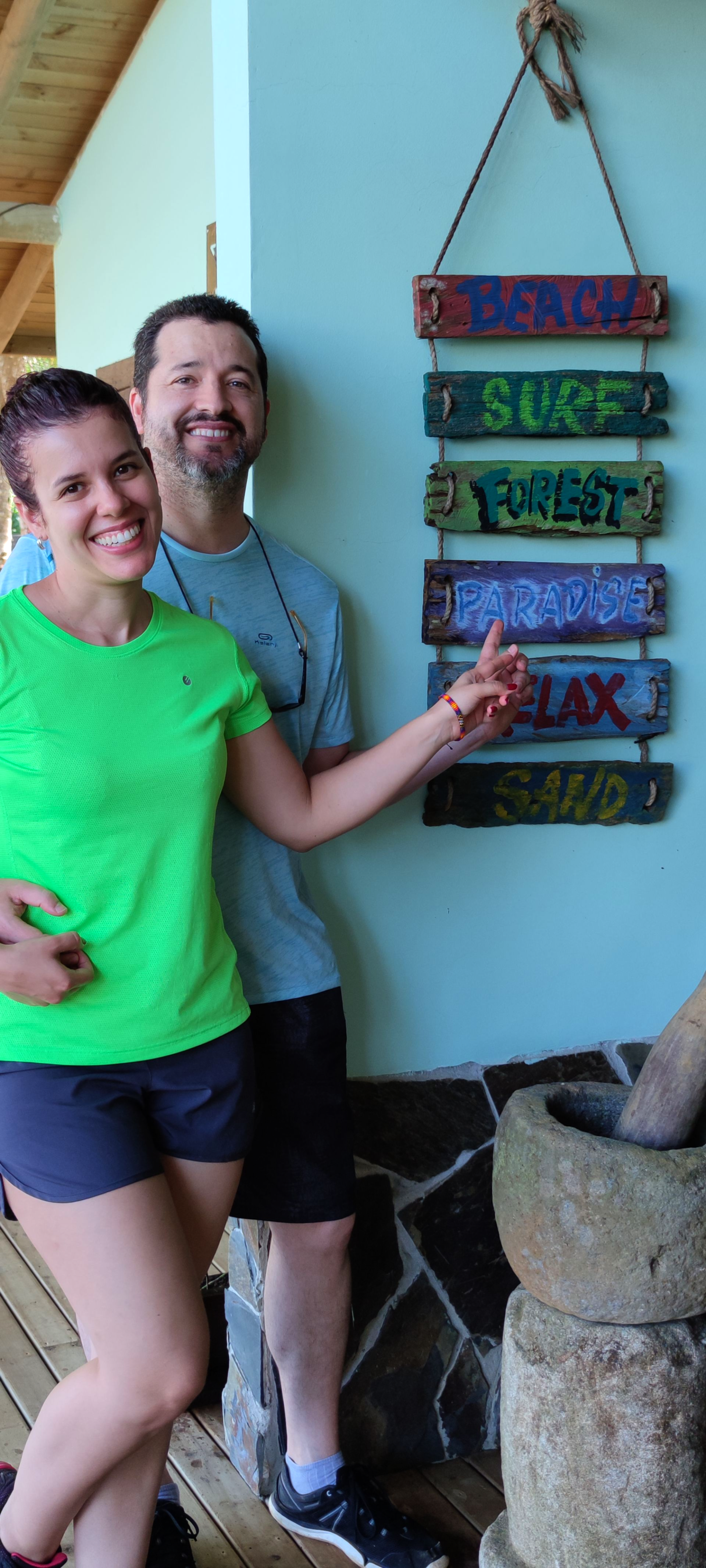 Two people smiling beside colorful hanging signs on a porch