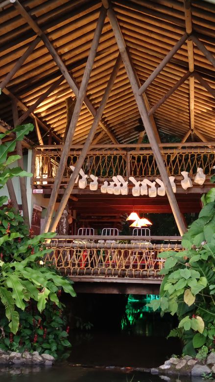 Tropical restaurant interior with thatched roof, wooden beams, hanging decor, and warm lighting above a dark entrance