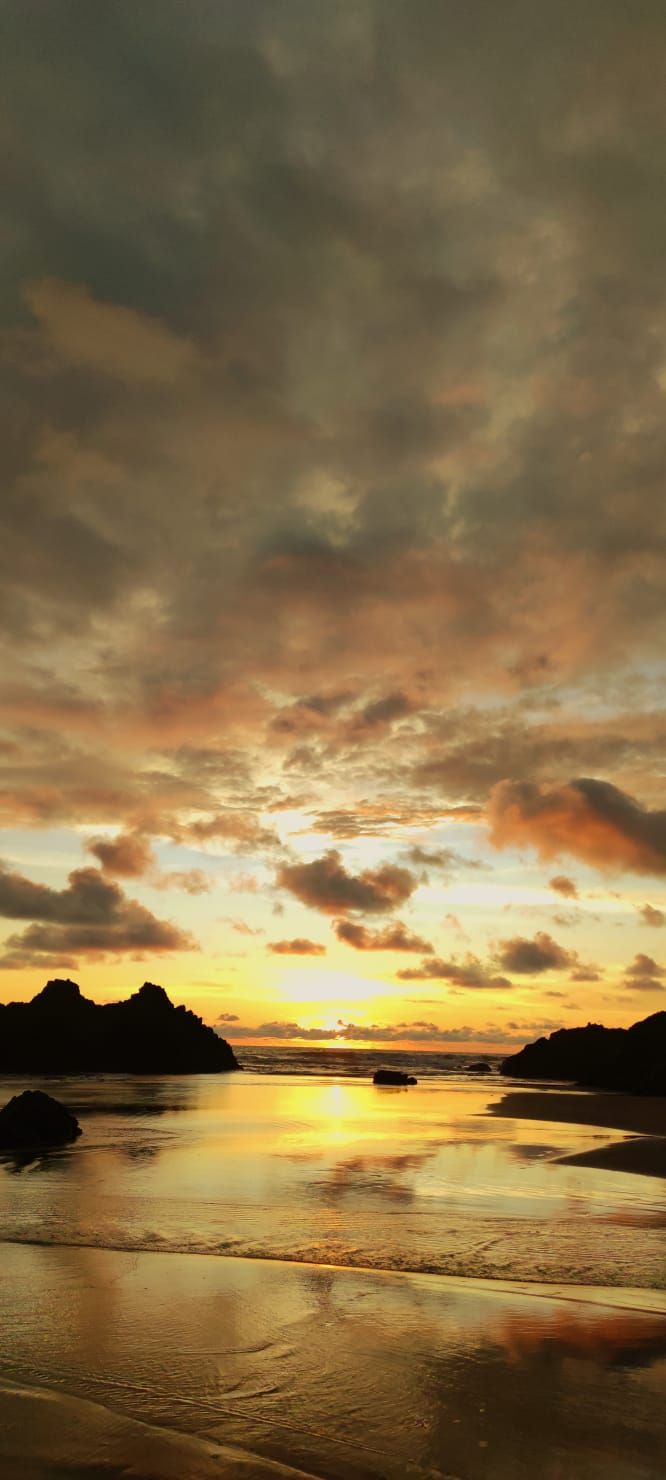 Sunset over a calm beach with glowing clouds and silhouetted islands reflected on wet sand