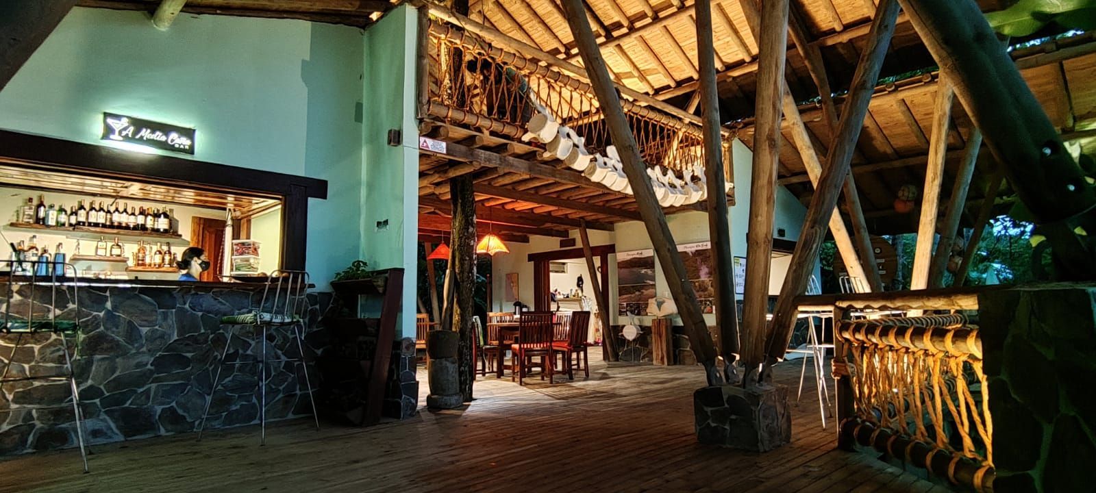Warmly lit rustic bar and lounge with wooden beams, stone counter, and seating area at night