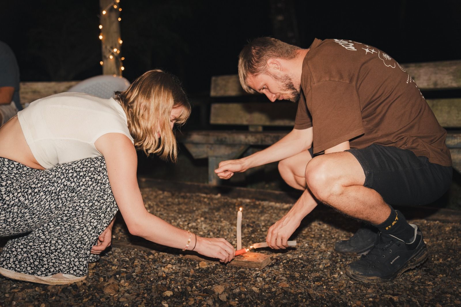 Two people kneeling outdoors, lighting a small sparkler on the ground at night