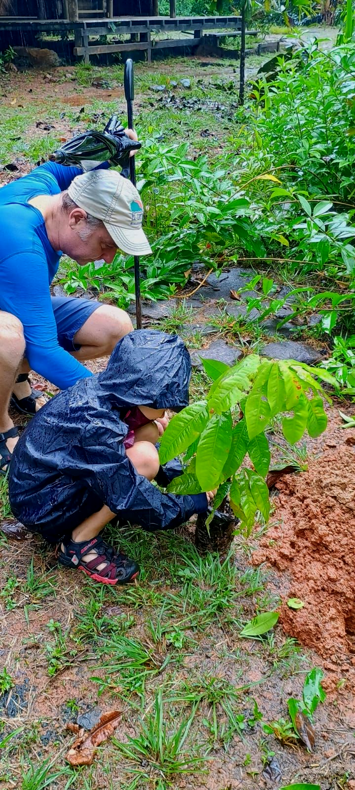 Two people kneeling and planting seedlings in a muddy garden bed.
