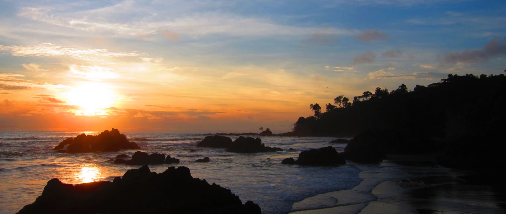 Sunset over rocky coastline with waves and orange sky