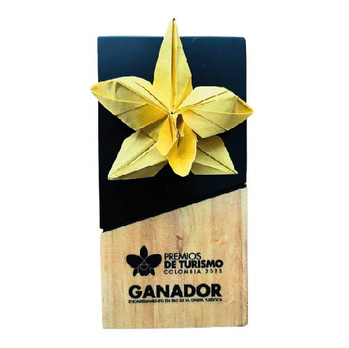 Yellow origami flower trophy on a wooden base labeled “GANADOR” with “Premios de Turismo” logo