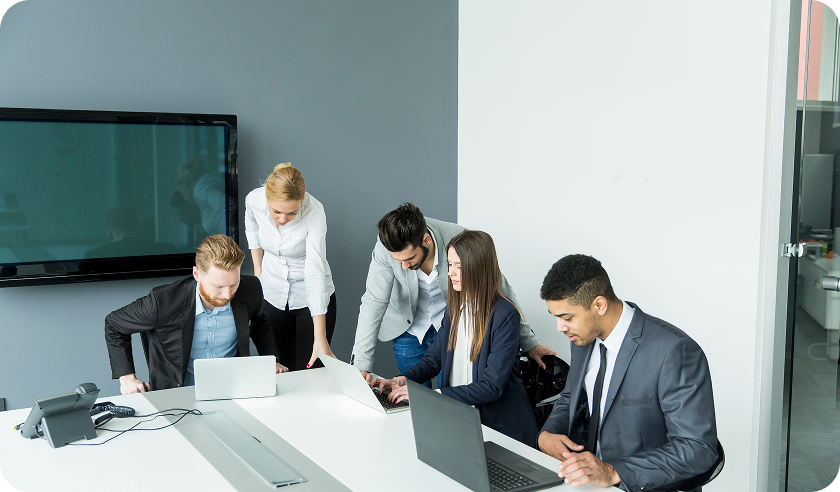 A group of business people are sitting around a table with laptops.