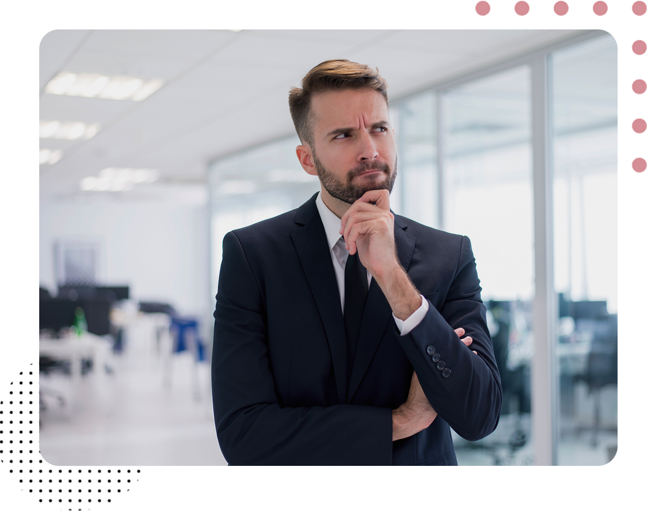 A man in a suit and tie is standing in an office with his hands on his chin.