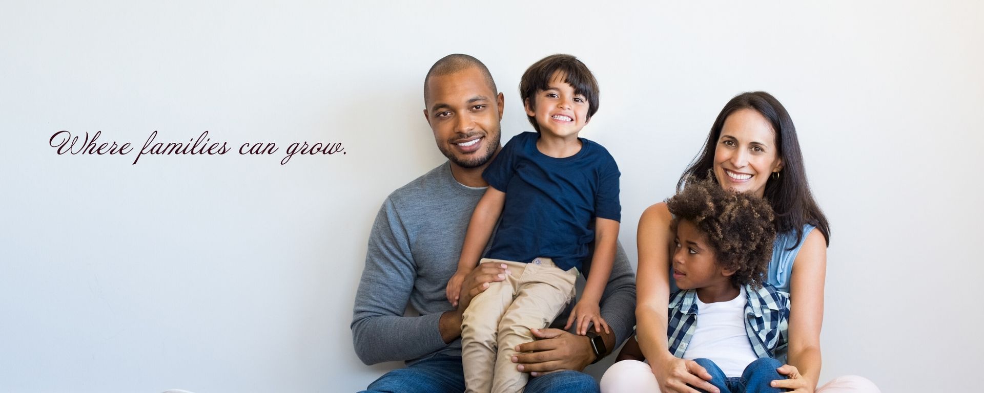 Family of four sitting together on a white background, smiling calmly.