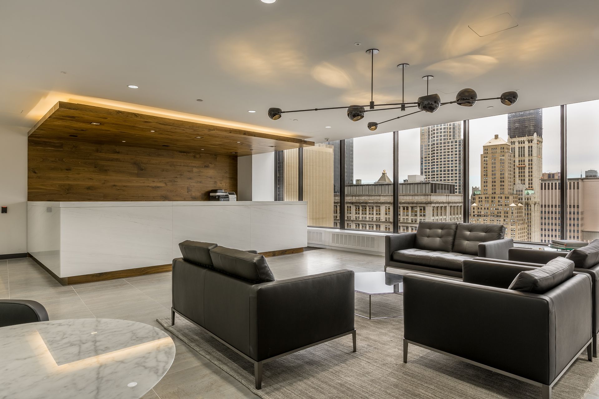 Modern office lobby with dark gray couches, white reception desk, city view.