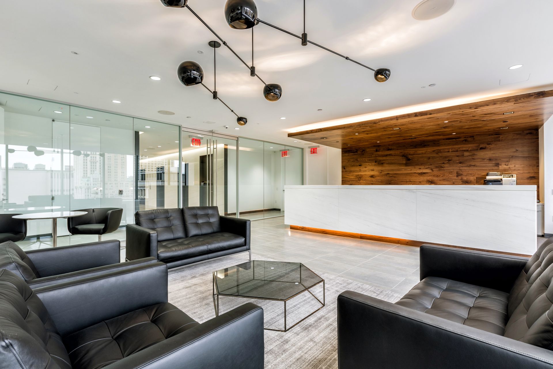 Modern office reception area with black leather couches, glass walls, and a wood-paneled reception desk.