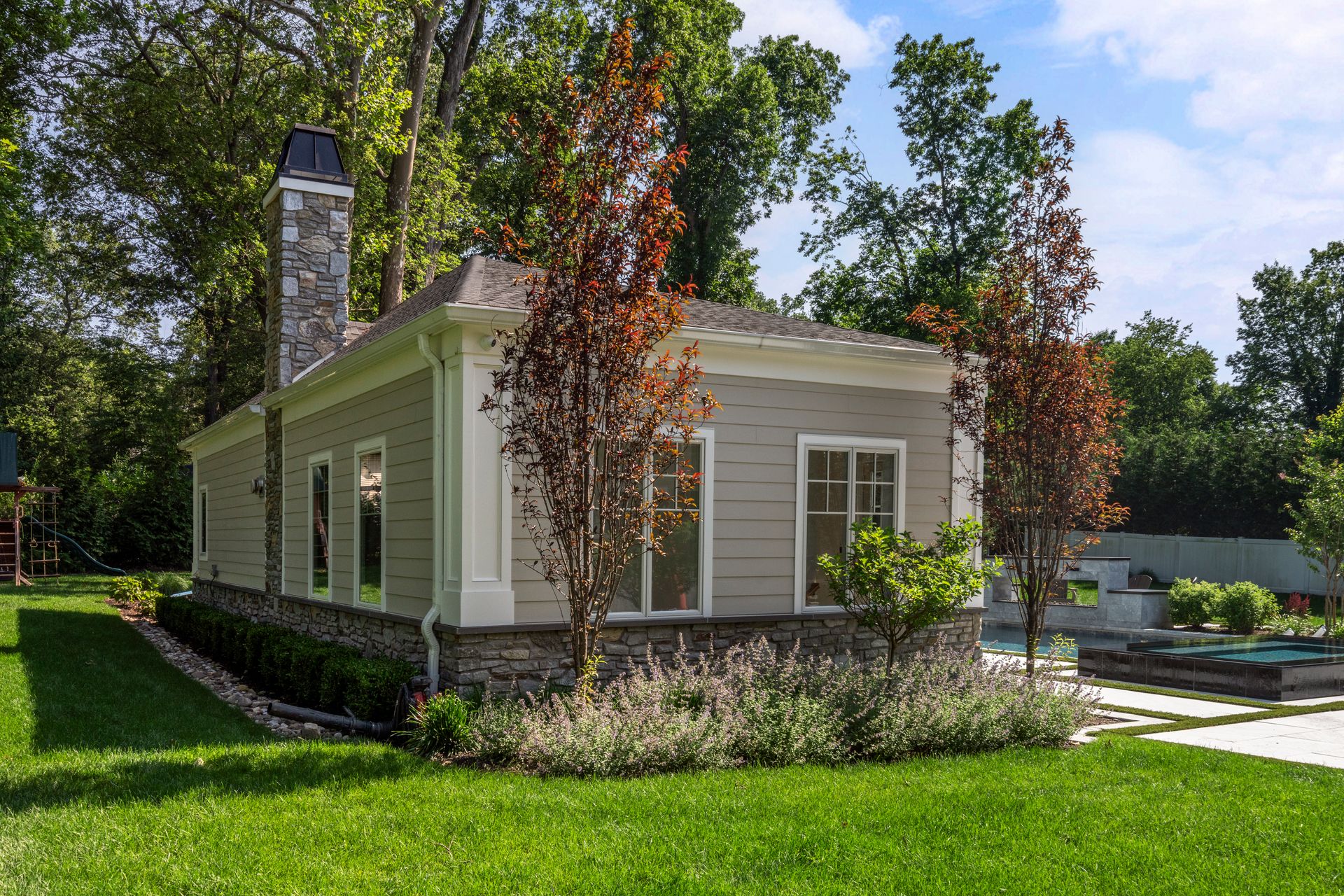 A light gray building with a stone chimney, surrounded by trees and green grass.