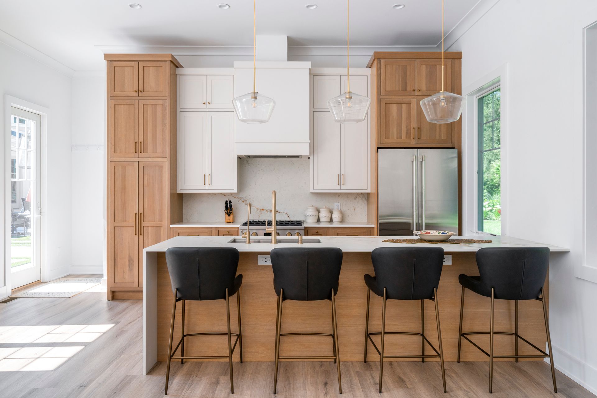 Modern kitchen with light wood cabinetry, stainless steel appliances, and island with black bar stools.