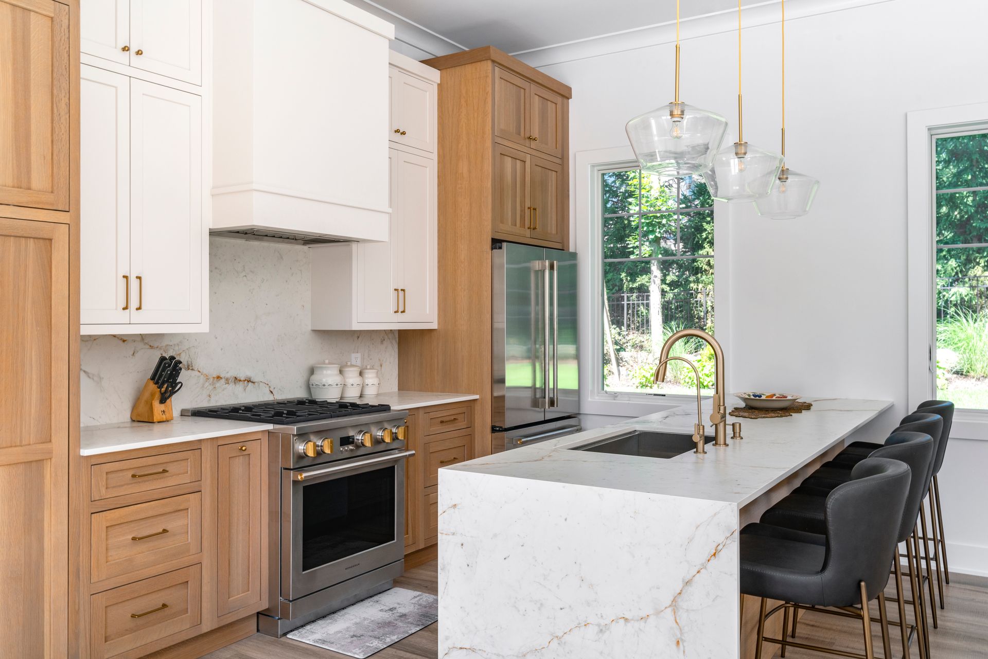 Modern kitchen with white and wood cabinets, marble countertops, stainless steel appliances, and a breakfast bar.
